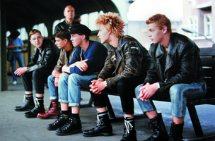 Szenenbild aus dem Dokumentarfilm &quot;flüstern &amp; SCHREIEN&quot;: Fünf junge Männer um die 20 sitzen auf einer Bank auf einem U-Bahnhof. Sie tragen Lderjacken, schwere Stiefel oder Punk-Frisuren. (© ICESTORM Entertainment GmbH)