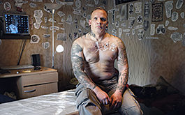 Alles andere zeigt die Zeit, Szenenbild: Ein Mann sitzt mit nackten und tätowierten Oberkörper auf einer Pritsche und blickt direkt in die Kamera. (© absolut Medien GmbH)