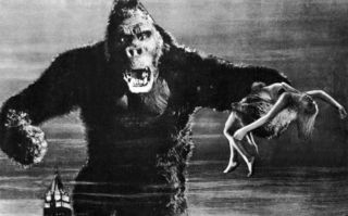 King Kong und die weiße Frau, Szenenbild aus dem Schwarz-Weiß-Film: Ein riesiger, Häuser überragender und bedrohlich aussehender Gorilla hält eine Frau in seiner linken Pranke.  (© IFTN/United Archives/picture alliance)