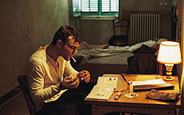Transit, Szenenbild: Georg sitzt am Schreibtisch in seinem Hotelzimmer und zündet sich eine Zigarette an. (© Schramm Film)