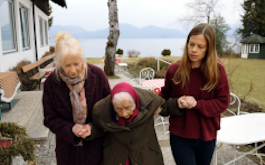 Walchensee Forever, Szenenbild: Eine alte Dame wird beim Gehen von ihrer Tochter und ihrer Enkeltochter gestützt. (© Flare Film)