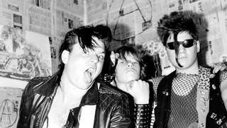 Schleimkeim – Otze und die DDR von unten, schwarz-weißes Szenenbild: Foto der Band Schleimkeim: drei junge Männer im Punk-Outfit, der Mann links steht die Zunge heraus. (© Arsenal Filmverleih)