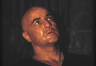 Szenenbild aus dem Film "Apcalypse Now Redux": Porträt eines glatzköpfigen Mannes – der Schauspieler Marlon Brando in der Rolle des Colonel Kurtz – vor dunklem Hintergrund. Der Mann sieht verschwitzt aus. (© picture alliance/United Archives)