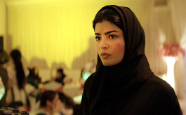 Die perfekte Kandidatin, Szenenbild: Eine junge Frau mit schwarzen Kopftuch steht in einem hell erleuchteten Saal. (© Neue Visionen)