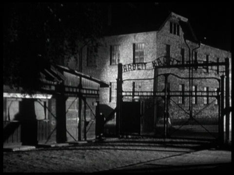 Nacht und Nebel, Filmstillin Schwarz-Weiß: Das Eingangstor von Auschwitz-Birkenau mit dem Schriftzug "Arbeit macht frei"
