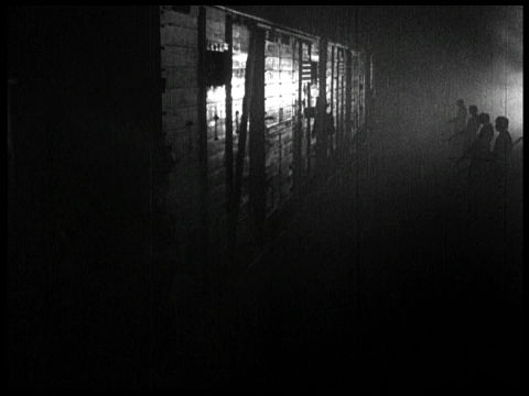Nacht und Nebel, Filmstill in Schwarz-Weiß: Nachtaufnahme eines Zuges, der von Soldaten bewacht wird