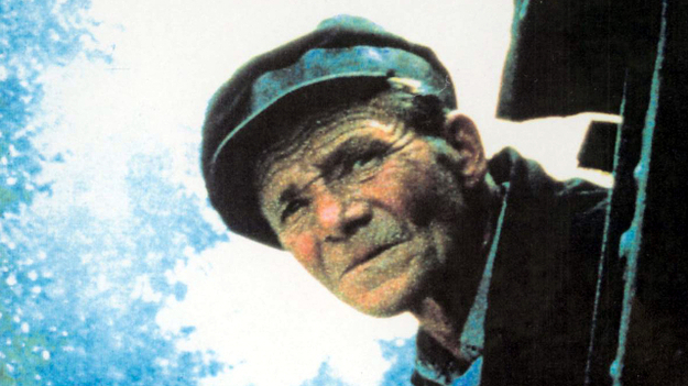 Shoah, Szenenbild: Ein alter Mann schaut aus einer Lok direkt in die Kamera. Unten links ist ein Schild mit dem Schriftzug "Treblinka" zu sehen. (© picture alliance / United Archives)