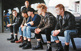 Flüstern &amp; Schreien, Szenenbild: Fünf junge Männer in Jeans und Springerstiefeln sitzen nebeneinander auf einer Bank auf einem Bahnsteig. (© DEFA Stiftung, Tina Bara)
