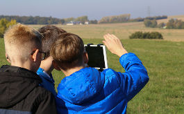 Drei Jungen, die am Projekt FILMmobil teilnehemn, filmen in einer ländlichen Landschaft mit einem Tablet (© Caroline Fuchs)