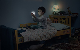 Der Mond und ich, Szenenbild: Ein kleiner Junge sitzt im Dunkeln in seinem Bett. Er hält eine kleine, strahlende Mondkugel in seinen Händen und betrachtet sie. (© ZDF)