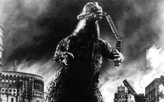 Godzilla, Szenenbild: Ein dinosauriermäßiges, riesiges Monster steht zwischen Häusern und verschlingt einen Eisenbahnzug. (© picture alliance / Everett Collection / Jerry Tavin)