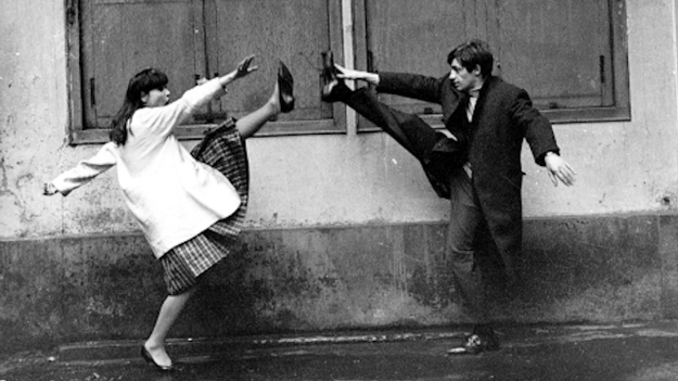 Eine Frau ist eine Frau, Szenenbild: Halbtotale: Eine Frau und ein Mann stehen sich gegenüber und reißen jeweils ein Bein in die Höhe. (© ddp images)