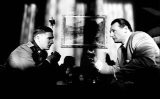 Schindlers Liste, Szenenbild in Schwarz-Weiß: Zwei Männer sitzen sich gegenüber. Der eine Trägt eine SS-Uniform. (© picture alliance/United Archives | United Archives / kpa Publicity)