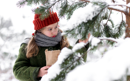 Weihnachten im Zaubereulenwald, Szenenbild: Nahaufnahme: Ein Mädchen im grünen Mantel und mit roter Mütze steht neben zugeschneiten Fichtenzweigen. (Foto: Kristjan Mõru © 2018 Luxfilm)