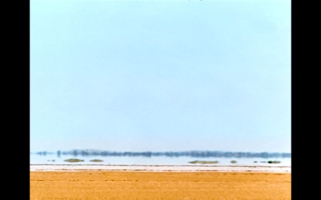 Fata Morgana, Szenenbild: Totale einer, in der Hitze flirrenden Wüstenlandschaft. Im Hintergrund ist ein Bus zu erkennen. (© Werner Herzog Film)
