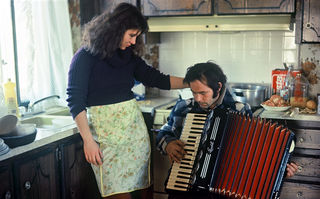 Stroszek, Szenenbild: Eine Frau mit Schürze steht in einer Küche neben einem sitzenden Mann, der ein Akkordeon hält. (© Werner Herzog Film)