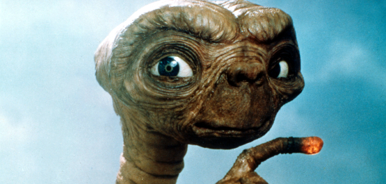 E.T. - Der Außerirdische, Szenenbild: Vor bläulichem Hintergrund ist die Titelfigur zu sehen: ein braunes, unbehaartes Wesen mit großer Stirn und langen Fingern. Sein Zeigefinger leuchtet. (© United Archives GmbH / Alamy Stock Photo)