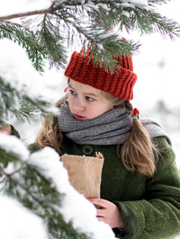 Weihnachten im Zaubereulenwald, Szenenbild: Nahaufnahme: Ein Mädchen im grünen Mantel und mit roter Mütze steht neben zugeschneiten Fichtenzweigen. (Foto: Kristjan Mõru © 2018 Luxfilm)