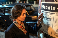 Ich bin! Margot Friedländer, Szenenbild: Eine junge Frau steht vor einer Lifaßsäule und ließt ein Werbeplakat für eine Theateraufführung (© ZDF und HARDY BRACKMANN)
