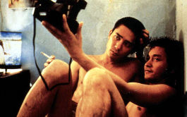 Happy Together, Szenenbild: Zwei nackte Männer sitzen aneinander geschmiegt auf dem Boden in einer Ecke. Sie machen ein Foto von sich selbst (© Picture Alliance United Archives)