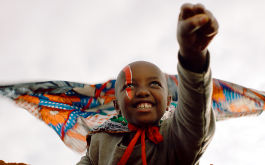 Supa Modo, Szenenbild: Ein kenianisches Mädchen reckt wie ein Superheld die Faust nach oben. Sie trägt einen flatternden Umhang. Über ihr rechtes Auge ist ein roter Streifen gemalt. (© One Fine Day Films)