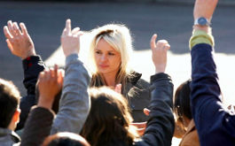 It's a Free World, Szenenbild: Eine blonde junge Frau steht vor einer Menschenmenge, die sich per Handzeichen melden. (© Neue Visionen)