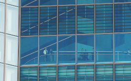 Oeconomia, Szenenbild: Gerasterte Glasfassade eines Hochhauses, in dem Menschen zu erkennen sind. (© Neue Visionen)