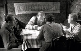 Kuhle Wampe, Szenenbild aus dem Schwarz-Weiß-Film: Eine Familie sitzt zusammen am Esstisch. Die Mutter kehrt dem/der Betrachtenden den Rücken zu. (© Praesens Film)