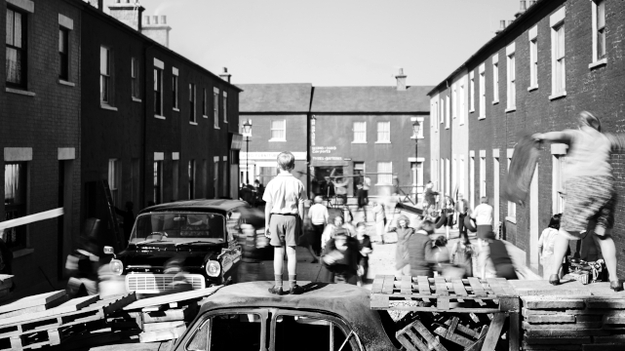 Belfast, Szenenbild: Blick in eine Wohnstraße. Im Vordergrund stehen Barrikaden, ein Junge steht auf einem Auto, mit dem Rücken zum Betrachtenden. ( © Rob Youngson / Focus Features)