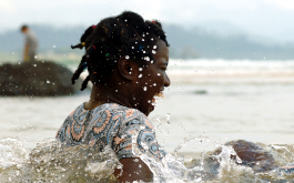 Warum ich euch nicht in die Augen schauen kann, Szenenbild: Ein Mädchen im Teenageralter badet lachend im Meer. (© DCM)