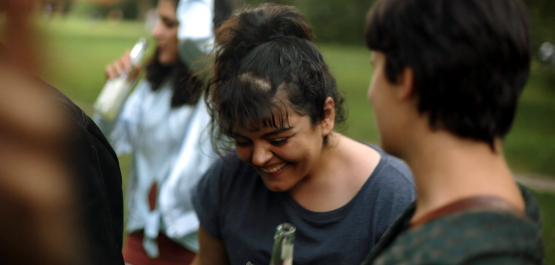 Nico, Szenenbild: Nahaufnahme Eine junge Frau stehend lachend in einer Gruppe von Gleichaltrigen. (© Darling Berlin / UCM.ONE)