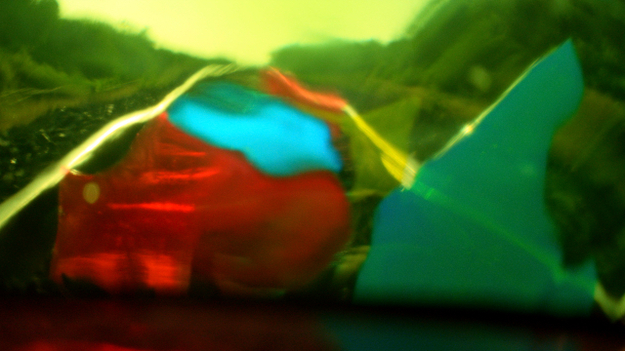 Das Licht, aus dem die Träume sind, Szenenbild: Verschiedene farbige Glasscherben sind zwischen ein Zuggleis gesteckt und verändern so die Farbigkeit der Lanschaft. (© Neue Visionen)