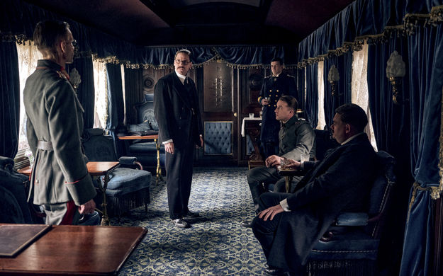 Im Westen nicht Neues (2022), Szenenbild: In einem eleganten dunklen Eisenbahnwagon stehen und sitzen fünf Männer, die in Anzügen und Uniformen gekleidet sind (© Netflix/Reiner Bajo)