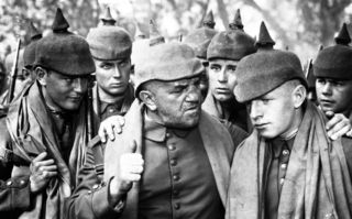Im Westen nichts Neues (1930), Szenenbild: Nahaufnahme in Schwarz-Weiß: Deutsche Soldaten mit Pickelhaube, in der Mitte steht ein älterer Soldat, der zu einem jüngeren Kameraden spricht. (© Capelight Pictures)