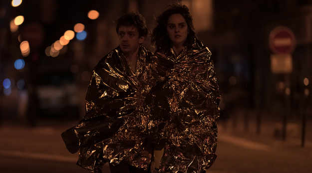 Frieden, Liebe und Death Metal, Szenenbild, frontal aufgenommen: Ein Mann und eine Frau laufen nachts nebeneinander in einer Straße. Sie sind in goldene Folien eingehüllt. (© Studiocanal)