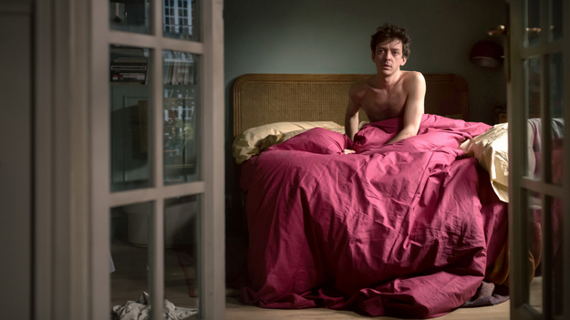Frieden, Liebe und Death Metal, Szenenbild, Halbtotale: Ein Mann sitzt mit nacktem Oberkörper in einem Bett. Die Bettwäsche ist rot. Der Abgebildete ist gerahmt von zwei Glastüren. (© Studiocanal)