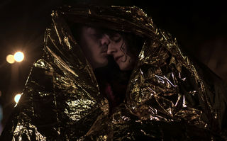 Frieden, Liebe und Death Metal, Szenenbild: Halbnah: Ein junger Mann und eine junge Frau halten ihre Köpfe aneinander. Sie sind in eine goldfarbene Folie eingewickelt. (© Studiocanal)