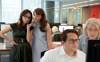 She Said, Szennebild: In einem Redaktionsraum: Zwei junge Frauen hören gemeinsam am Handy einem Telefonat zu. Im Vordergrund sitzt ein Mann vor einem Computer, neben ihm beugt sich eine ältere Frau dem Bildschirm zu. (© Universal Pictures 2022)