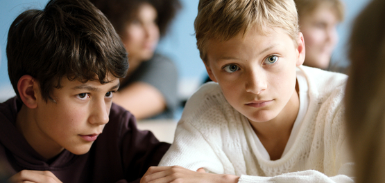 Close, Szenenbild: Nahaufnahme: Zwei Jungen im Teenageralter – der eine dunkelhaarig, der andere blond – sitzen in einem Klassenraum nebeneinander und hören jemanden zu. (© Pandora Film)