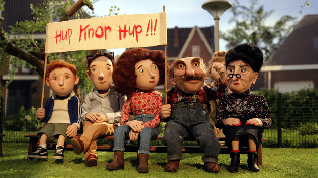 Oink, Szenenbild aus dem Puppentrickfilm: Auf einer Bank sitzen fünf Figuren unterschiedlichen Alters. Sie halten ein Plakat in die Höhe. (© Kinostar Filmverleih GmbH)