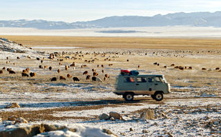 Checker Tobi und die Reise zu den fliegenden Flüssen, Szenenbild: Ein Kleinbus fährt durch eine weite, zum Teil verschneite Ebene in der Mongolei. (© megaherz film und fernsehen)