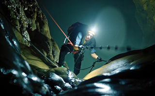 Checker Tobi und die Reise zu den fliegenden Flüssen, Szenenbild: Checker Tobi klettert in einer dunklen Höhle auf die Betrachtenden zu. Er trägt eine Lampe an seinem Helm. (© megaherz film und fernsehen)