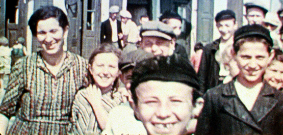 Szenenbild aus dem Film "Three Minutes – A Lengthening": Drei Kinder und eine Frau blicken lächelnd in die Kamera. Im Hintergrund sind weitere Menschen zu erkennen. Das Bild wurde 1938 in einer polnischen Kleinstadt aufgenommen. (© US Holocaust Memorial Museum)