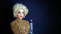 Land of Dreams, Szenenbild: Porträt einer jungen Frau mit blonder Perücke, die in ein Oberteil mit Leopardenmuster trögt; sie stet vor einem dunklen Hintergrund (W-film / Ghasem Ebrahimian / Bon Voyage Films / Palodeon Pictures)