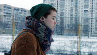 Stop Zemlia, Szenenbild: Nahaufnahme: Ein Mädchen mit Mütze auf dem Kopf läuft im Winter vor Hochhäusern entlang. (© Oleksandr Roshchyn)