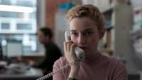 The Assistant, Szenenbild: Nahaufnahme einer jungen blonden Frau, die einen Telefonhörer an ihr Ohr hält. (© Forensic Films/Ascot Elite)