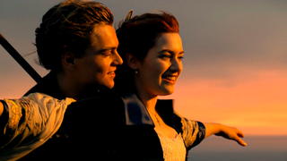 Titanic, Szenenbild: Ein junger Mann steht hinter einer jungen Frau und umarmt sie, während sie die Arme ausbreitet. Hinter dem Paar ist der abendrote Himmel über dem offenen Meer zu sehen (© Walt Disney Studios Motion Pictures Germany)