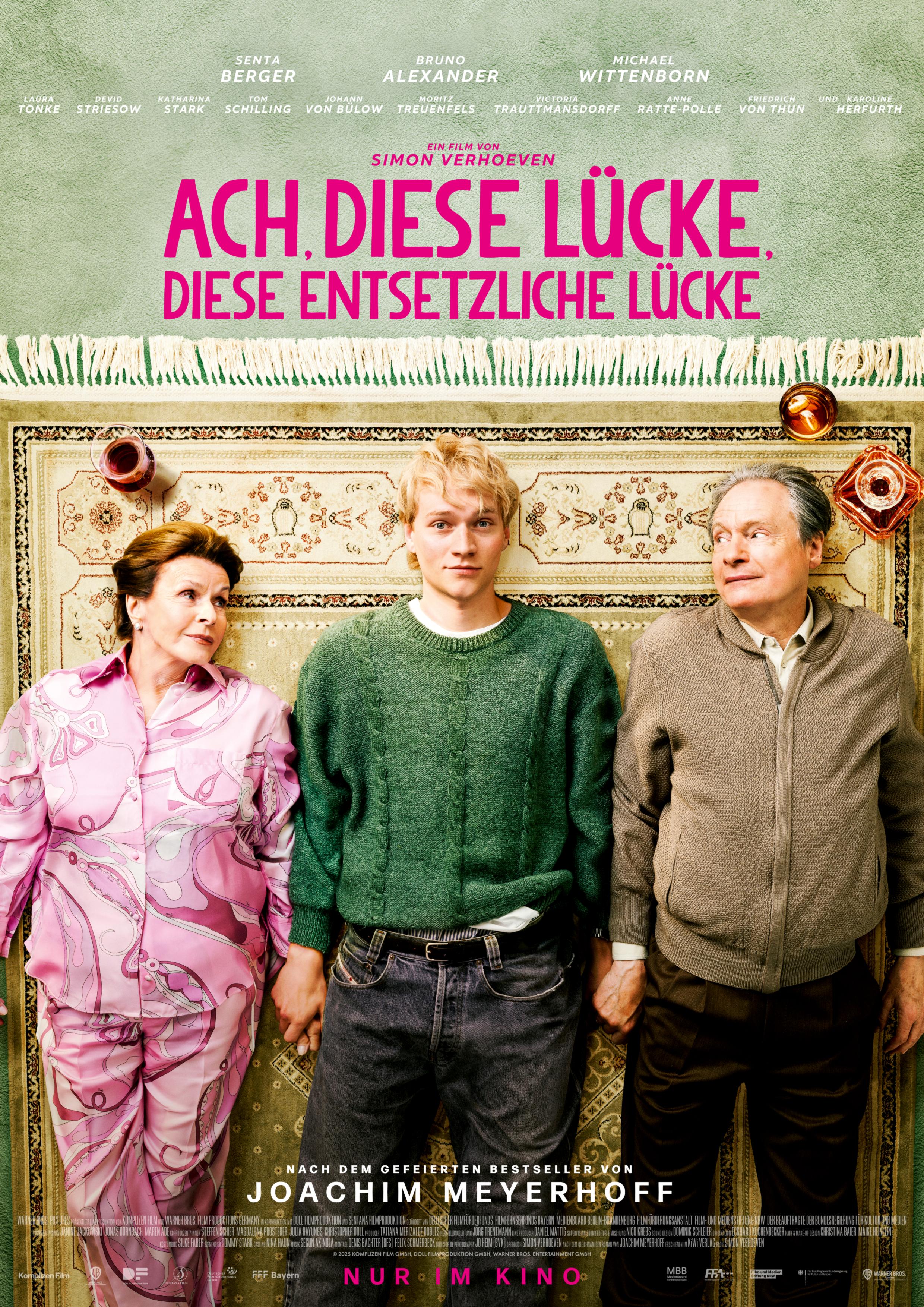 Filmplakat zum Spielfilm ACH, DIESE LÜCKE, DIESE ENTSETZLICHE LÜCKE: Ein junger Mann zwischen zwei seinen Großeltern liegt auf dem Teppich. Die beiden Alten schauen ihn, das Bild ist von oben aufgenommen. Darüber steht in Pink der Filmtitel.