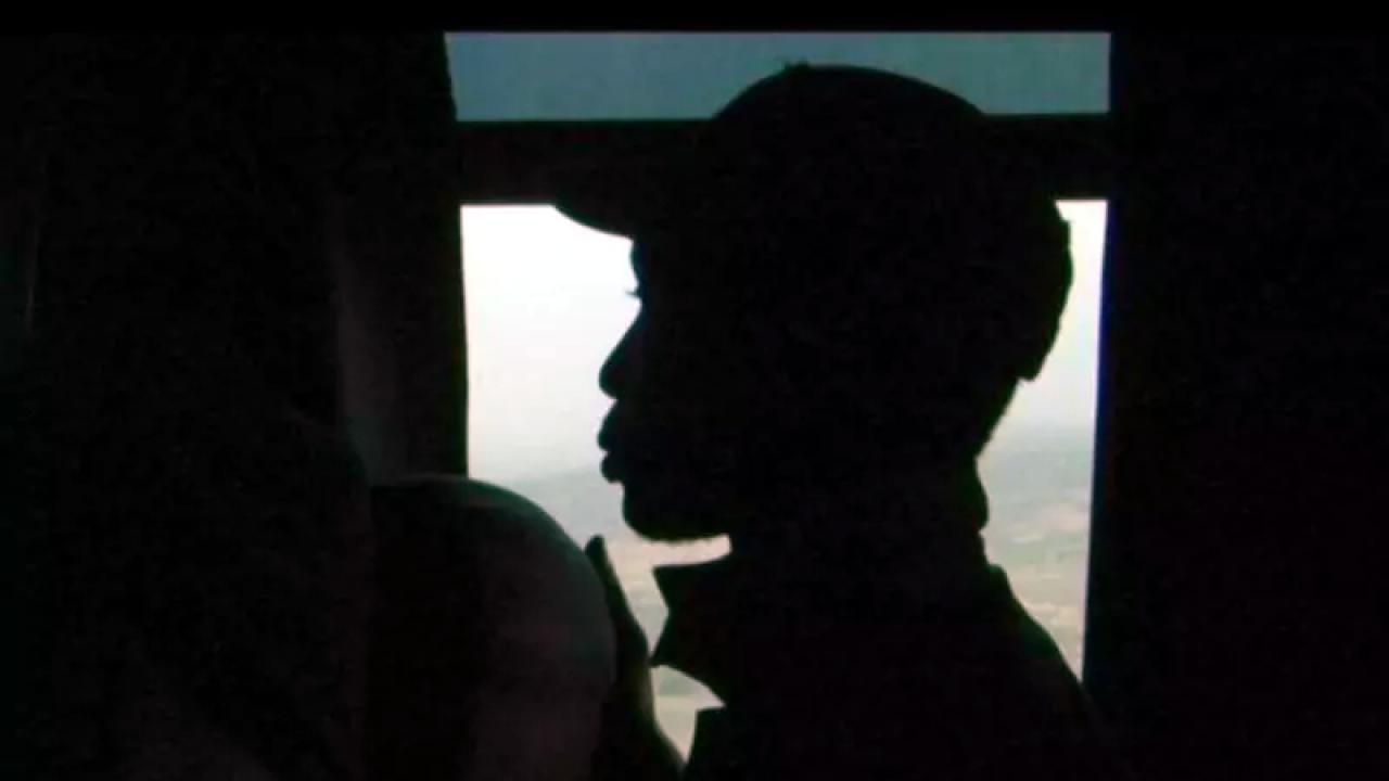 Szenenbild aus dem Dokumentarfilm "Fremd": Im Gegenlicht ist die Silhouette eines Mannes vor einem Fenster zu sehen, der ein Basecap trägt