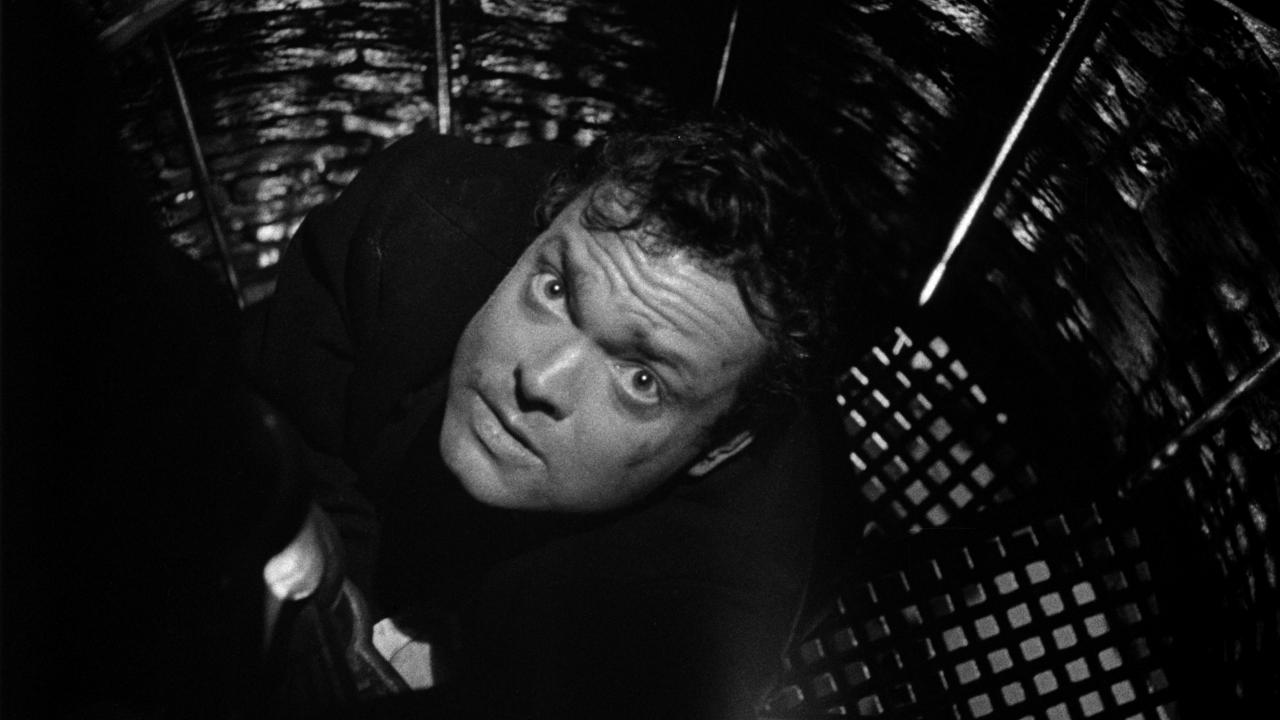 Szenenbild aus dem Thriller DER DRITTE MANN: Halbnahaufnahme eines Mannes auf einer dunklen Wendeltreppe nach oben in Richtung Kamera schaut